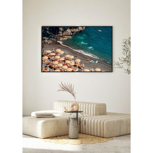 May include: An aerial view of a beach with turquoise water, a rocky cliff, and a line of orange and white beach umbrellas.
