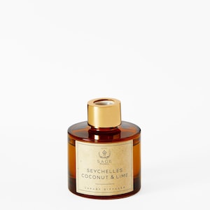 Può includere: Una bottiglia di vetro marrone con un tappo dorato e un'etichetta che recita "SAGE BOTANICALS SEYCHELLES COCONUT & LIME LUXURY DIFFUSER".