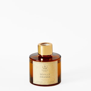Könnte beinhalten: Eine braune Glasflasche mit goldenem Deckel und einem Etikett mit der Aufschrift "SAGE BOTANICALS SEVILLE ORANGE LUXURY DIFFUSER".
