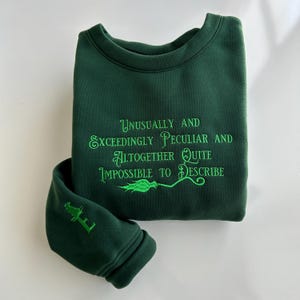 May include: Green sweatshirt with the text "Unusually and Exceedingly Peculiar and Altogether Quite Impossible to Describe" embroidered in green.