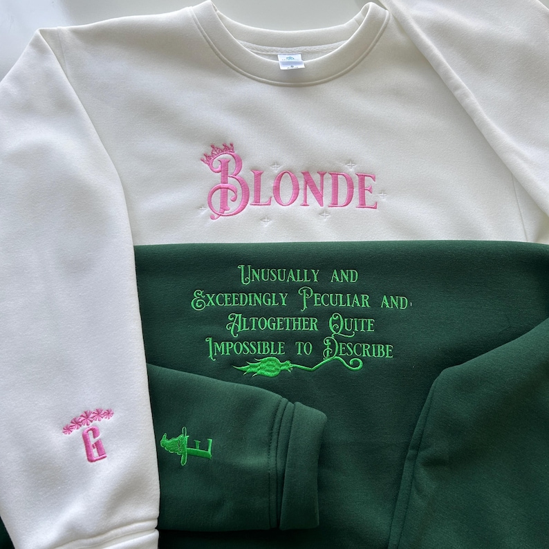 May include: A white sweatshirt with pink embroidery that says "BLONDE" with a crown above the "B". The sweatshirt is layered over a green sweatshirt with green embroidery that says "UNUSUALLY AND EXCEEDINGLY PECULIAR AND ALTOGETHER QUITE IMPOSSIBLE TO DESCRIBE".