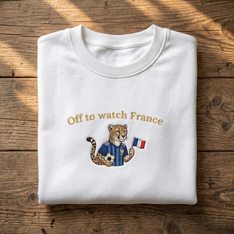 Peut inclure: Sweat-shirt blanc avec la phrase brod&eacute;e "Off to watch France". Le motif repr&eacute;sente un gu&eacute;pard portant un maillot de foot bleu, tenant un ballon et un drapeau fran&ccedil;ais. Le sweat-shirt a un col rond.