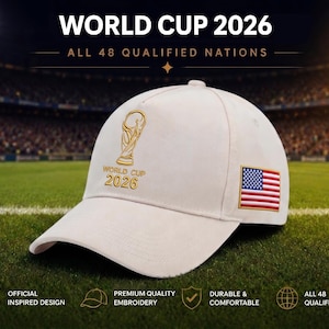 May include: A light beige baseball cap featuring gold embroidery of the World Cup 2026 trophy and text on the front. The side of the cap displays a rectangular patch of the United States flag with red, white, and blue stripes and white stars.