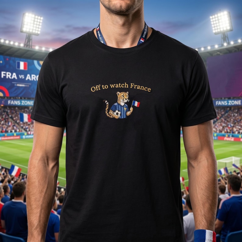 Peut inclure: T-shirt noir avec l'inscription dor&eacute;e "Off to watch France". Le t-shirt pr&eacute;sente un gu&eacute;pard de dessin anim&eacute; portant un maillot de football bleu et tenant un ballon de football et un drapeau fran&ccedil;ais. Le fond montre un stade de football.