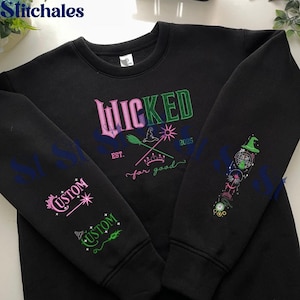 May include: Black sweatshirt with the word "WICKED" in pink and green, along with a witch's hat, broom, and the words "EST. for good 2025." The sleeves feature the word "CUSTOM" in pink and green, and a design with a witch's hat and other elements.