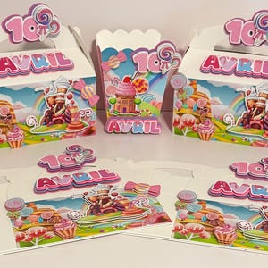 Puede incluir: Cajas de regalo y un recipiente para palomitas de maíz blancos con temática de dulces, con ilustraciones coloridas de un país de caramelos. Las cajas tienen el nombre "AVRIL" y el número "10". Decoradas con piruletas y caramelos.