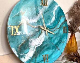 May include: A large round clock with a turquoise and white abstract design. The clock face has Roman numerals and gold-coloured hands.