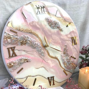 Può includere: Orologio da parete rotondo con cornice bianca, caratterizzato da un design astratto rosa, bianco e oro. I numeri romani segnano le ore. Le lancette dell'orologio sono dorate. L'orologio ha una finitura in resina ed elementi decorativi.