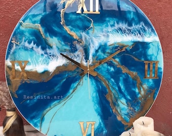 May include: A large, round clock with a blue and white resin art design. The clock face features Roman numerals and gold accents. The text "Resinita.art" is visible on the clock face.