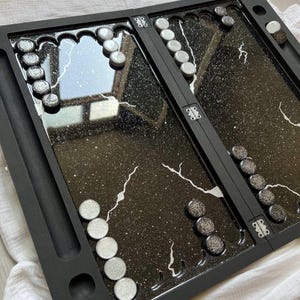 May include: A black and white marble-patterned backgammon board with silver glitter. The board is closed and the pieces are arranged in the starting positions.