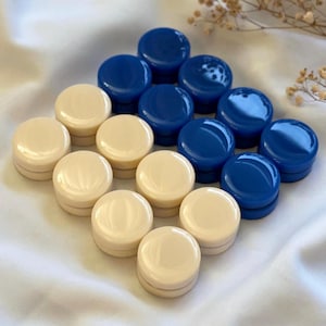 May include: An assortment of cream and blue game pieces arranged in a diamond pattern. The pieces are round with a flat top and a slightly raised edge. The cream-colored pieces alternate with the blue ones.