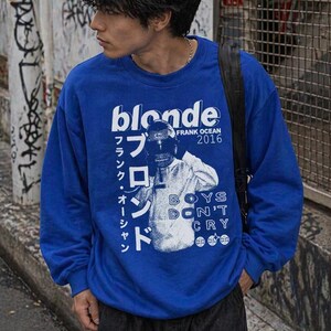 May include: A royal blue sweatshirt with the word "blonde" in white block letters. The sweatshirt also features the text "FRANK OCEAN 2016" and Japanese text. A black and white graphic is also visible.