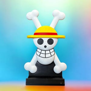 May include: A white skull with a yellow and red straw hat, wearing a black base. The skull has a toothy grin and black eyes.