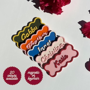 May include: Five colourful personalised name tags with wavy edges. The names are Gabby, Heather, Janet, Christina, and Katie. The tags are available in 20 colours and can be attached with a magnetic or keychain.