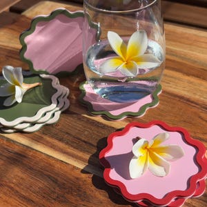 May include: Three different coloured coasters with scalloped edges. Each coaster features a pink, green, or red base with a white rim. A white flower is placed on each coaster.