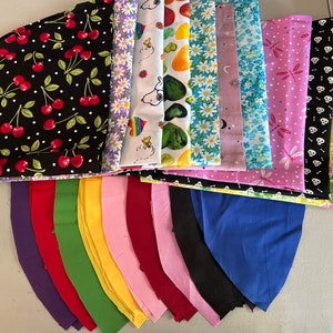 Könnte beinhalten: Eine Sammlung von Stoffresten in verschiedenen Farben und Mustern, darunter Kirschen, Blumen, Totenköpfe und geometrische Muster. Die Stoffe sind in einer Halbkreisform angeordnet, wobei die größeren Stücke oben und die kleineren Stücke unten liegen.