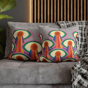 Peut inclure: Deux coussins gris avec un motif rétro coloré. Le motif présente un motif répétitif de formes en forme d'œil avec des rayures arc-en-ciel orange, jaune, vert, rose, violet et bleu. Les coussins sont sur un canapé gris.