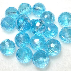 May include: A collection of faceted, light blue crystal beads. The beads are round with multiple facets that catch the light, creating a sparkling effect. The beads are a pale, translucent blue color.