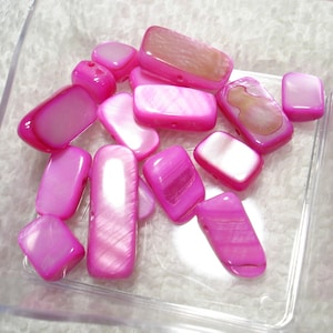 May include: A collection of pink and white shell beads with iridescent shimmer. The beads are rectangular and have a smooth, polished finish.