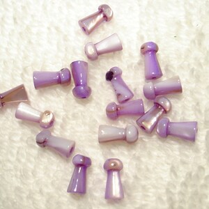 May include: A collection of 18 purple and white shell beads with a mushroom shape. The beads have a pearlescent finish.