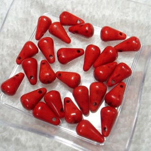 May include: A collection of red teardrop-shaped beads in a clear plastic container. The beads are smooth and have a slightly glossy finish.