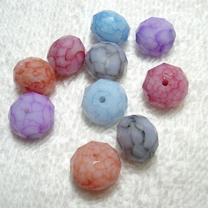 May include: Assortment of ten faceted glass beads with a marbled effect. The beads are in shades of pink, purple, blue, and white.