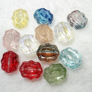 May include: A collection of colorful, decorative glass beads in various shades including yellow, blue, pink, brown, clear, red, and green. Each bead has a unique, wavy, oval shape with a hole for stringing. The beads are ideal for jewelry making and crafts.