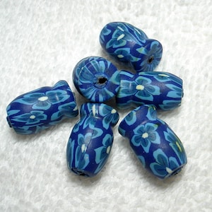 May include: Six blue and white floral patterned ceramic beads. The beads are oval shaped and have a hole in the center.