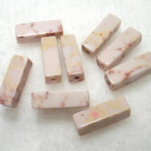 May include: A collection of rectangular beads in shades of pink and cream, with reddish-brown veining. The beads have a polished finish and are drilled with holes for stringing. These beads are ideal for jewelry making.