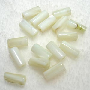 May include: A collection of off-white, cylindrical beads with a glossy finish. The beads are scattered on a light-colored surface. Some beads have subtle variations in color and texture, suggesting a natural material.