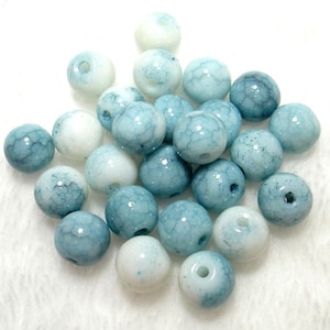 May include: A collection of round beads in shades of blue and white. The beads have a marbled appearance with visible veining. Each bead has a hole for stringing. The beads are suitable for jewelry making.