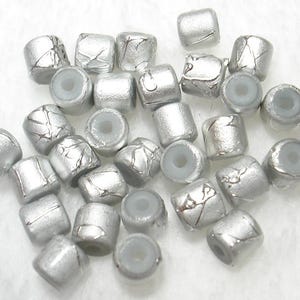 May include: A collection of silver-colored, barrel-shaped beads with a crackled, textured finish. Each bead has a light gray center hole. These beads are suitable for jewelry making and crafting projects.