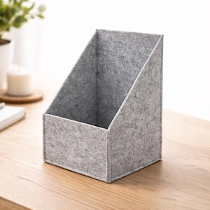 Puede incluir: Un revistero de fieltro gris con base rectangular y respaldo inclinado. El organizador está diseñado para guardar revistas, archivos u otros documentos. El color neutro y el diseño sencillo lo hacen adecuado para cualquier oficina o decoración del hogar.