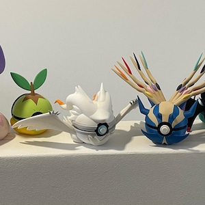 May include: A row of colourful, stylised figurines with distinct designs. The figurines, made of plastic, are arranged in a line, displaying a range of shapes and colours, including yellow, pink, green, white, blue, black, orange, and purple. The figurines are on display.