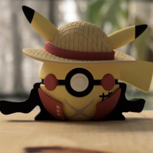 Puede incluir: Una figura amarilla de Pikachu con un sombrero de paja con una banda roja, gafas redondas rojas y un atuendo rojo y negro. La figura está sobre una superficie de madera.