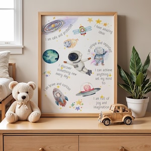 Może przedstawiać: Biały plakat z motywem kosmicznym przedstawiający astronautę, rakietę, UFO i gwiazdy. Plakat zawiera pozytywne afirmacje, takie jak "Jestem bezpieczny i chroniony", "Mam niesamowite pomysły", "Jestem wyjątkowy i ważny", "Odkrywam coś nowego każdego dnia", "Jestem odważny i ciekawy", "Mogę osiągnąć wszystko, co sobie postanowię", i "Jestem pełen radości i wyobraźni".