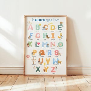 May include: A framed alphabet art print with the text "In GOD'S eyes, I am." Each letter is illustrated with a corresponding word and image, such as "A" for "accepted" and "B" for "beloved." The artwork features pastel colours and whimsical illustrations.