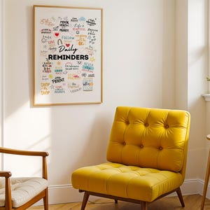 May include: A framed white poster with colourful handwritten text that reads "Daily Reminders" and includes words like "love", "follow", "patient", "never", "keep calm", "be kind", "live without regrets", and "going with the flow". The poster is hanging on a white wall above a yellow armchair.