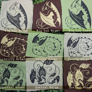 May include: Nine fabric squares with different color combinations of beige, brown, and green. Each square features a stylized black and white illustration of a dragon. The text on each square reads "Big Guy Beige", "Big Guy Brown", "Big Guy Green", "Pointy Brown", "Pointy Green", "Pointy Beige", "Quetzal Green", "Quetzal Beige", and "Quetzal Brown".