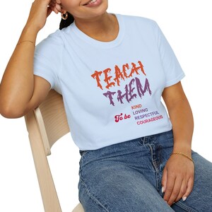 May include: A light blue t-shirt with the text "Teach Them To Be Kind Loving Respectful Courageous" in a stylized font. The text is in orange, red, and purple.