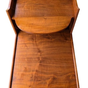 May include: A brown wooden side table featuring a rectangular top surface and a lower shelf with a curved front edge. The piece is constructed with vertical side panels that connect the two levels, showcasing a natural wood grain finish throughout.