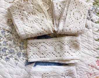 May include: Four folded strips of off-white and white lace trim featuring intricate circular floral patterns and scalloped edges. The lace pieces vary in width and texture, showcasing detailed needlework with openwork designs and delicate thread borders.