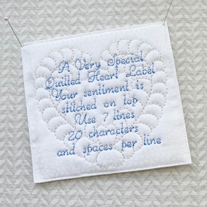 May include: A white quilted heart-shaped label with blue embroidery that reads "A Very Special Quilted Heart Label Your sentiment is stitched on top Use 7 lines 20 characters and spaces per line".