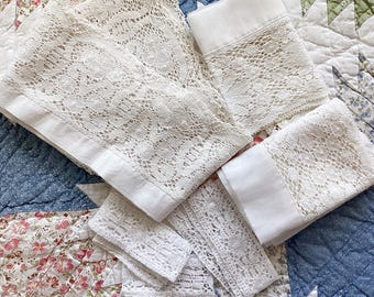 May include: A collection of off-white lace trim pieces featuring intricate floral patterns and scalloped edges. The set includes several rectangular strips of varying lengths, each finished with a smooth, solid fabric border along one side.