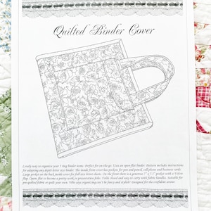 May include: Line drawing of a quilted binder cover with a floral pattern. The cover has a handle and a pocket. Text at the top reads "Quilted Binder Cover". The image is on a white background with decorative borders.