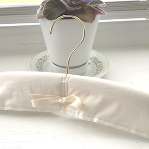 May include: A white padded hanger with a gold metal hook. The hanger is designed for delicate clothing.