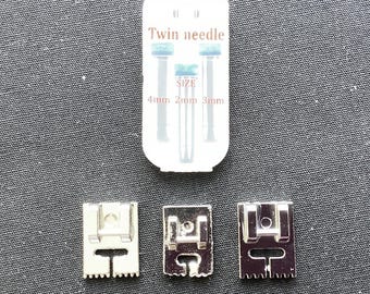 May include: A clear plastic case labeled Twin needle with 4mm, 2mm, and 3mm size indicators, accompanied by three silver-colored metal sewing machine presser feet. The presser feet feature a rectangular shape with a central slot and serrated edges.
