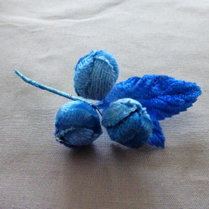 May include: A blue velvet flower with three blooms and a single leaf. The flower is made of soft, plush fabric and has a vintage look.