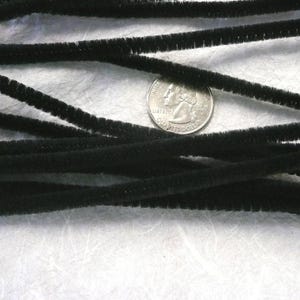 May include: A close-up of a bundle of black pipe cleaners. The pipe cleaners are arranged in a criss-cross pattern and are about the same length as a US quarter.