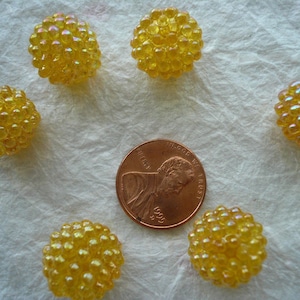 May include: Six yellow iridescent glass buttons with a textured surface. The buttons are arranged in a circle on a white background.